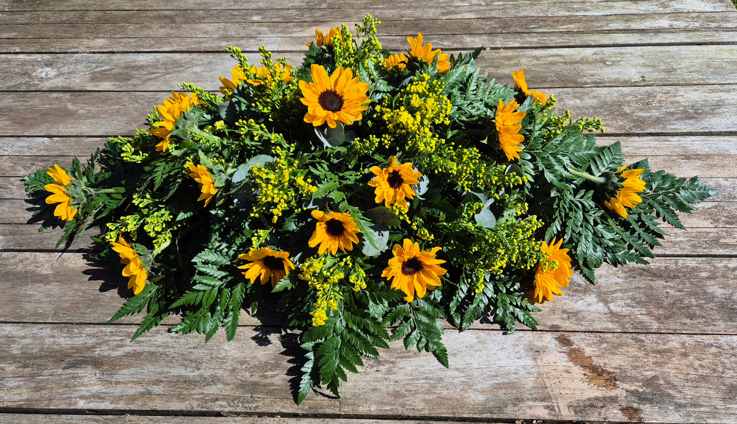 Funeral coffin spray with greenery and sunflowers on a wooden background