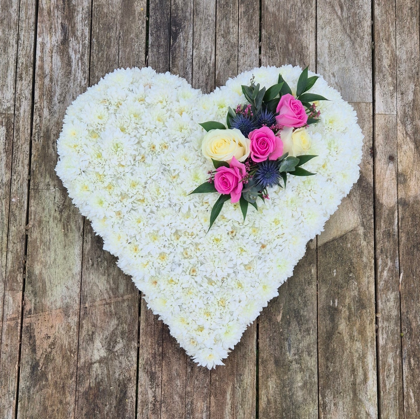 Heart-shaped arrangement of white flowers with pink and yellow accents on a wooden background