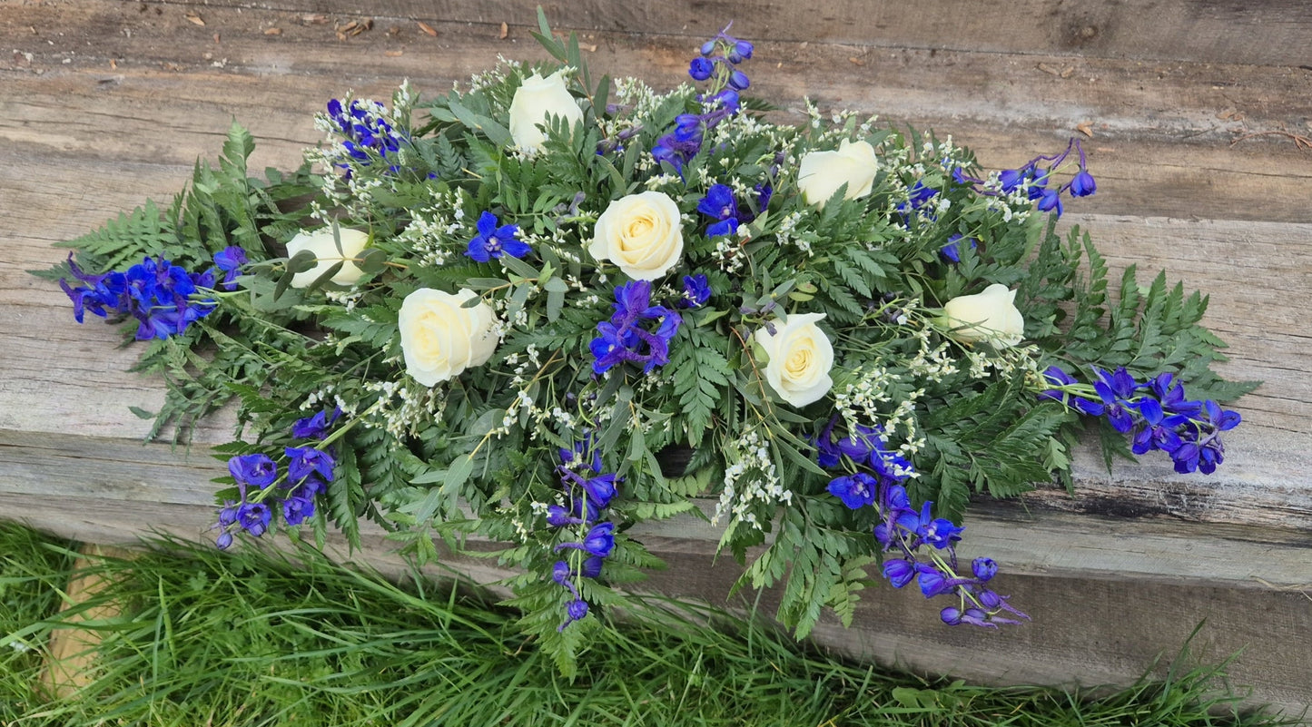 Funeral coffin spray with greenery and colourful flowers on a wooden background