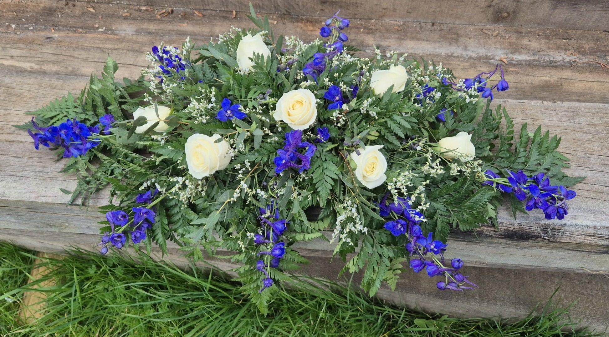 Funeral coffin spray with greenery and colourful flowers on a wooden background