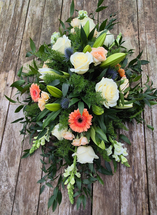 Funeral coffin spray with greenery and colourful flowers on a wooden background