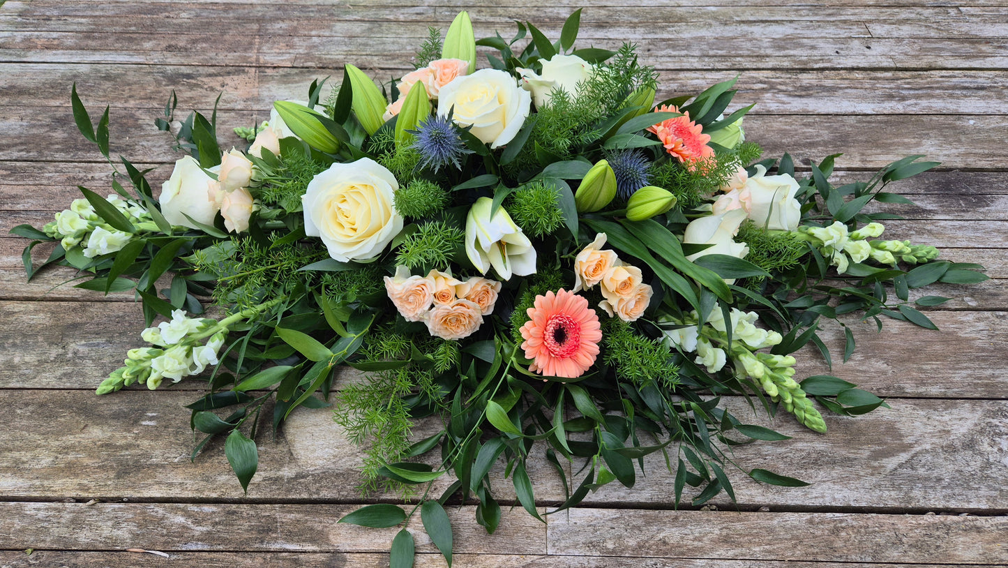 Funeral coffin spray with greenery and colourful flowers on a wooden background