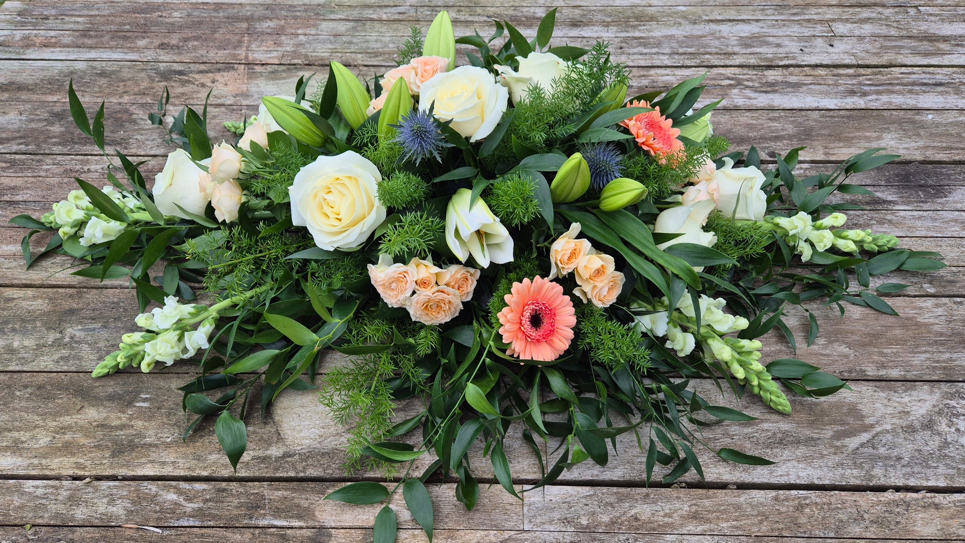 Funeral coffin spray with greenery and colourful flowers on a wooden background